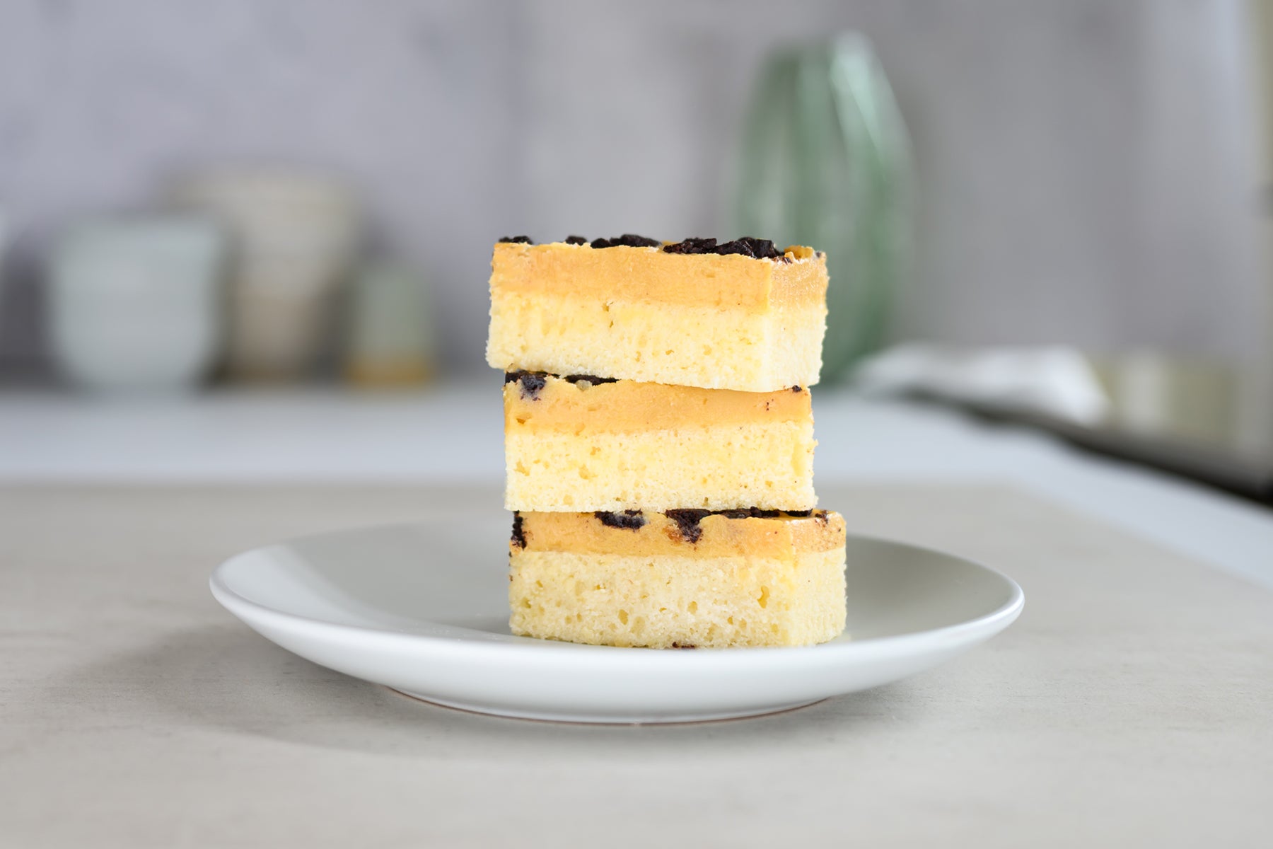 Stack of three square pastries on a white plate with a blurred background. Dessert Kitchen Desserts About us