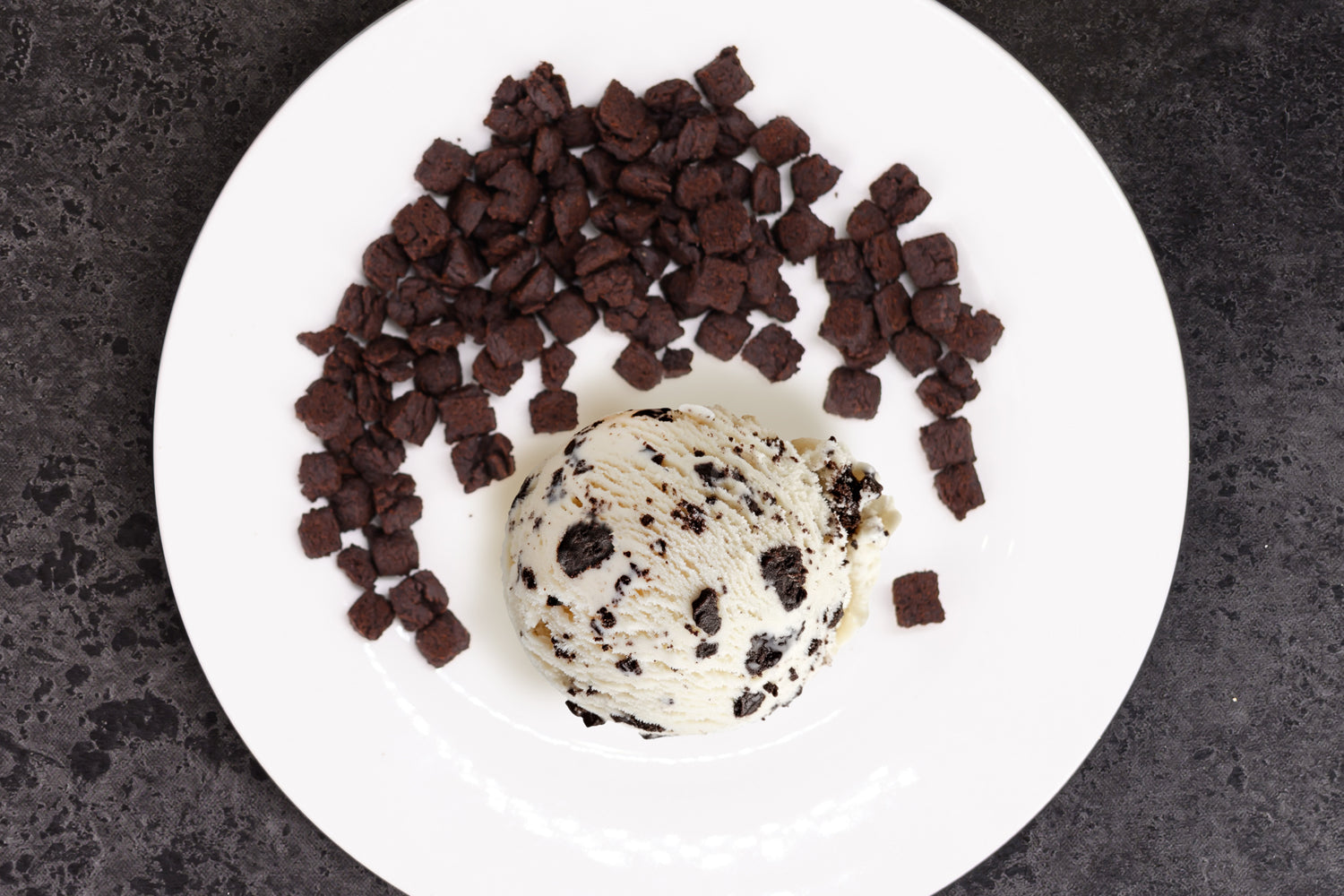 Ice cream scoop with chocolate chips on a white plate against a dark background. Dessert Kitchen Inclusions