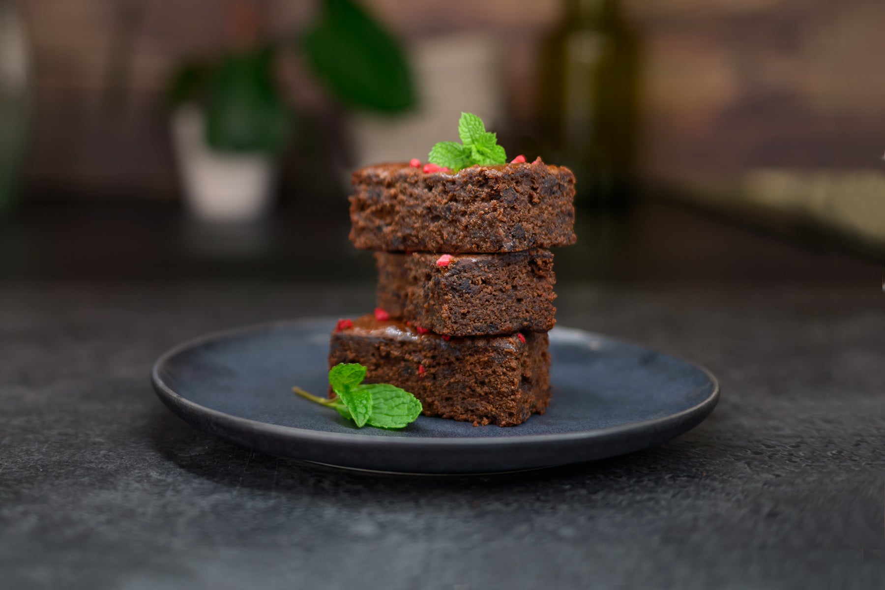 Three brownies stacked on a dark plate with green leaves on a dark background. Dessert Kitchen Desserts