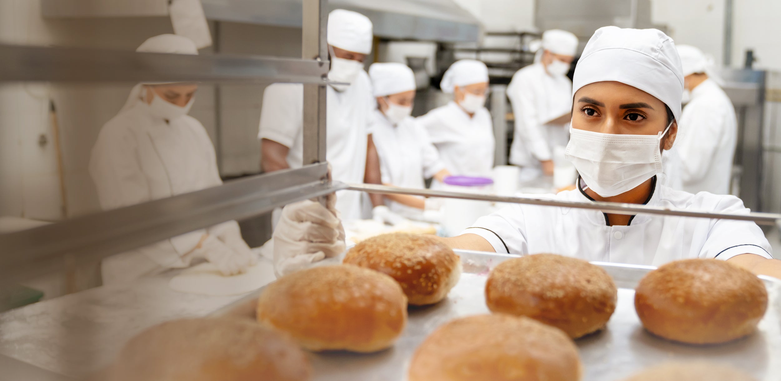 Commercial bakers working in a bakery with bread on a conveyor belt. Dessert Kitchen