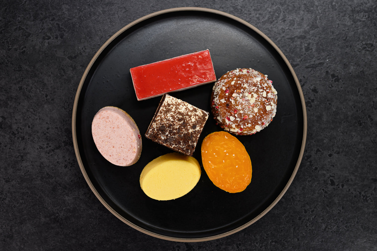 Assorted colorful candies on a black plate against a dark background. Dessert Kitchen Innovation Services