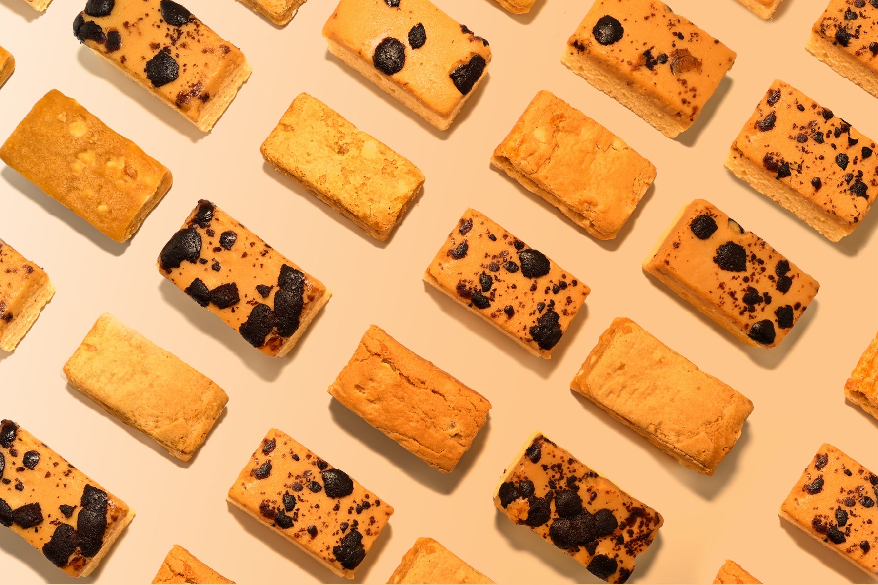 Pattern of rectangular cookies with chocolate chips on a beige background. Dessert Kitchen Partner Manufacturing