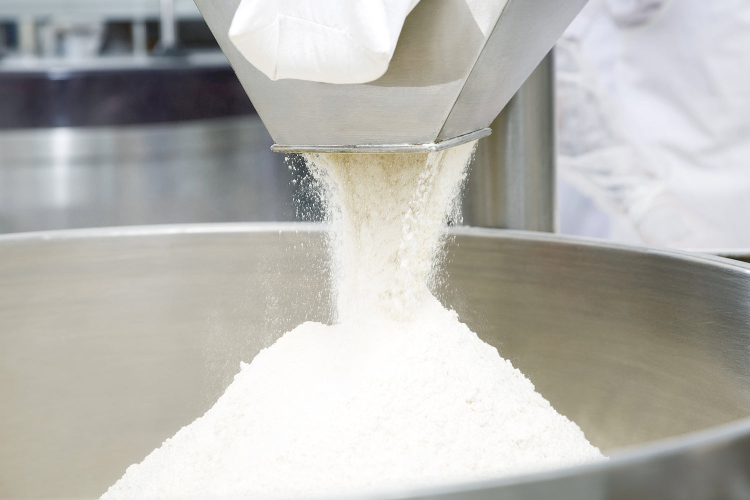 White powder being poured from a container into a large metal bowl. Dessert Kitchen Ingredients