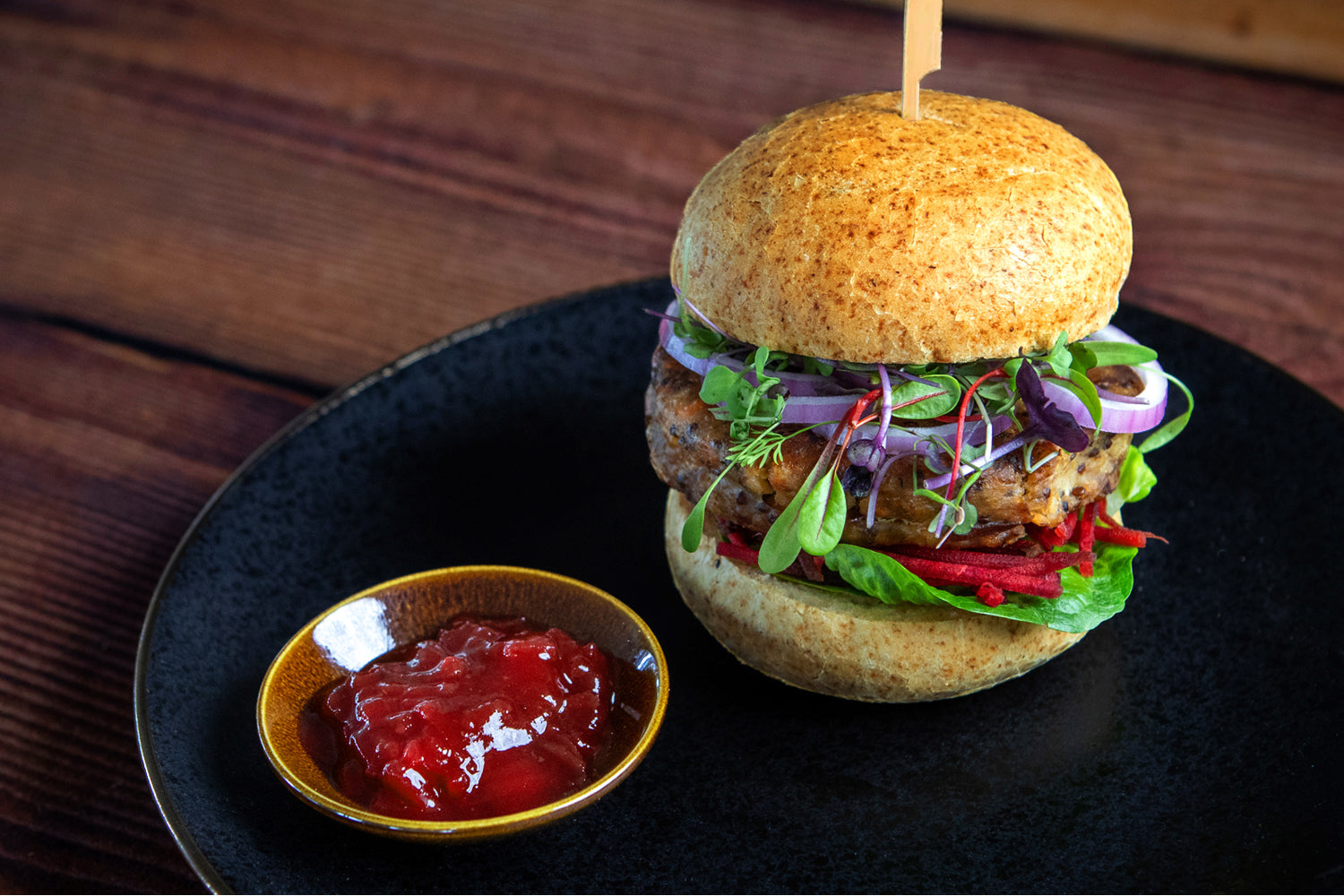 Hamburger with ketchup on a black plate on a wooden table. Dessert Kitchen Gluten Free Bread & Buns