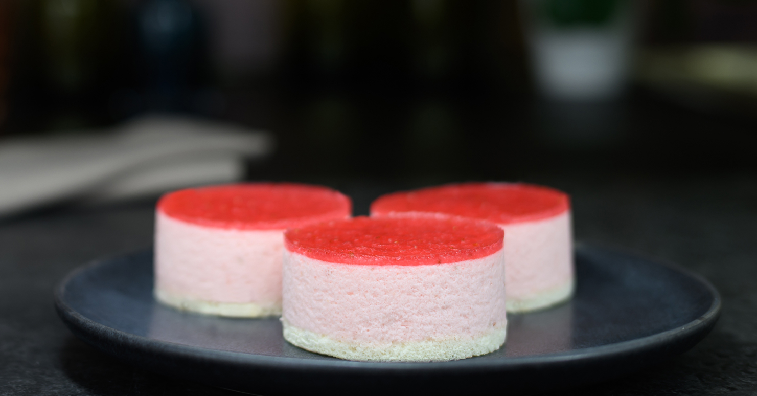 Three small round desserts with red and white layers on a dark plate.