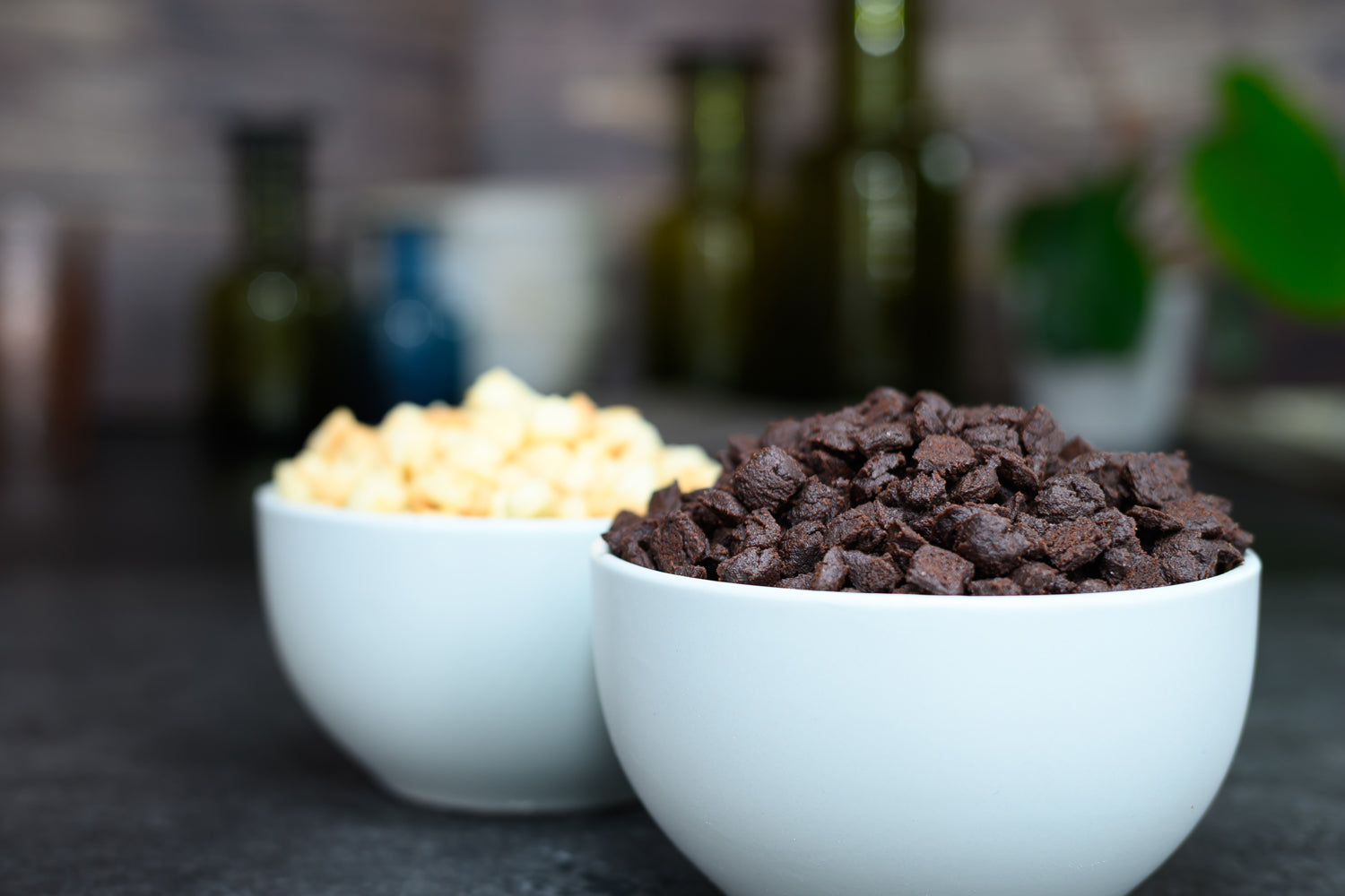 Two white bowls with one containing light-coloured inclusion pieces and the other dark-coloured inclusion pieces on a blurred kitchen background. Dessert Kitchen