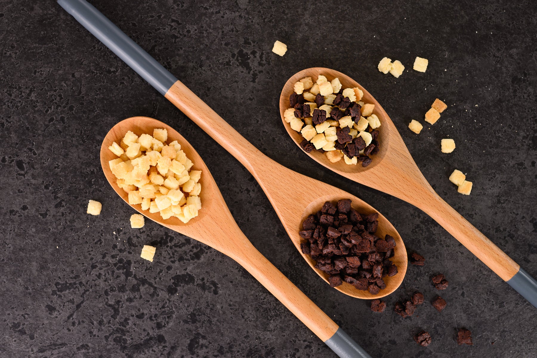 Three wooden spoons filled with different types of food inclusions on a dark surface. Dessert Kitchen