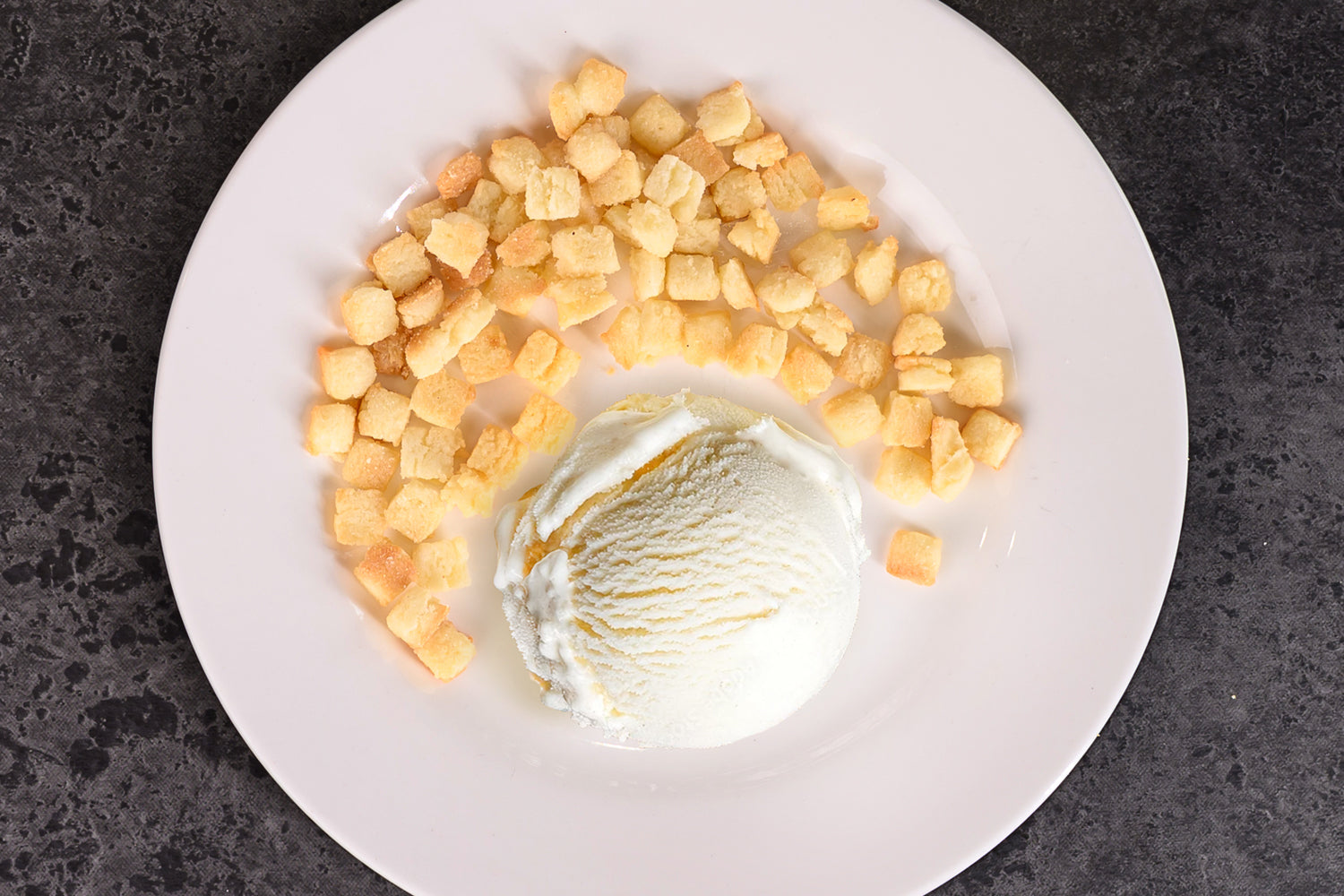 Ice cream scoop with food inclusion chunks on a white plate against a dark background. Dessert Kitchen