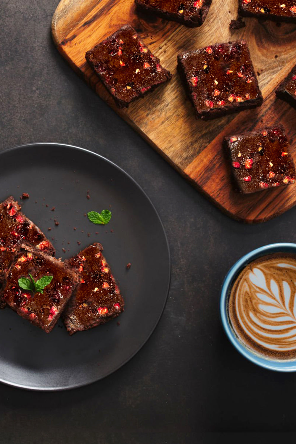 Brownies on a wooden cutting board with a plate and coffee cup on a dark surface. Dessert Kitchen