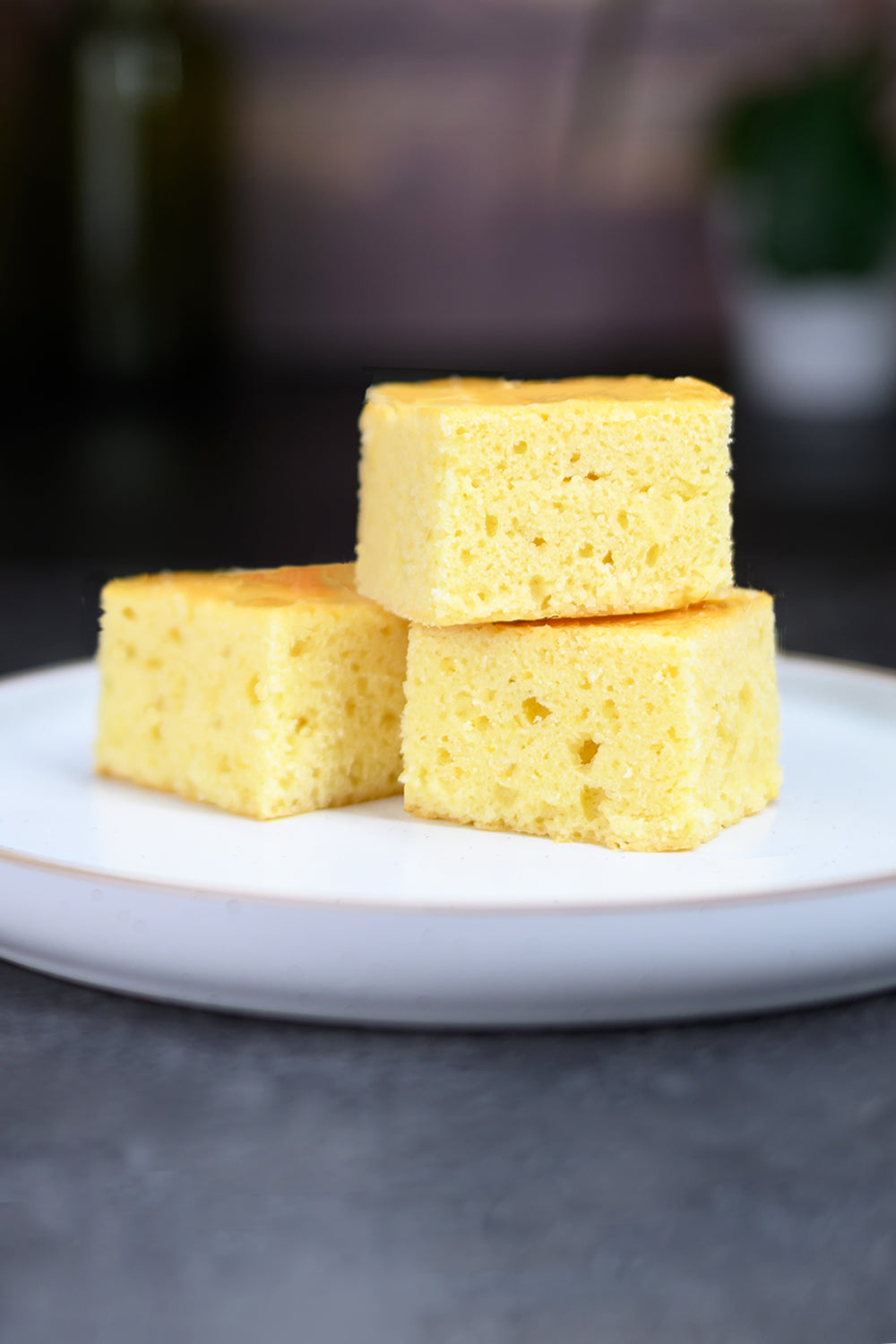 Three pieces of yellow spongecake stacked on a white plate with a blurred background. Dessert Kitchen Partner Manufacturing