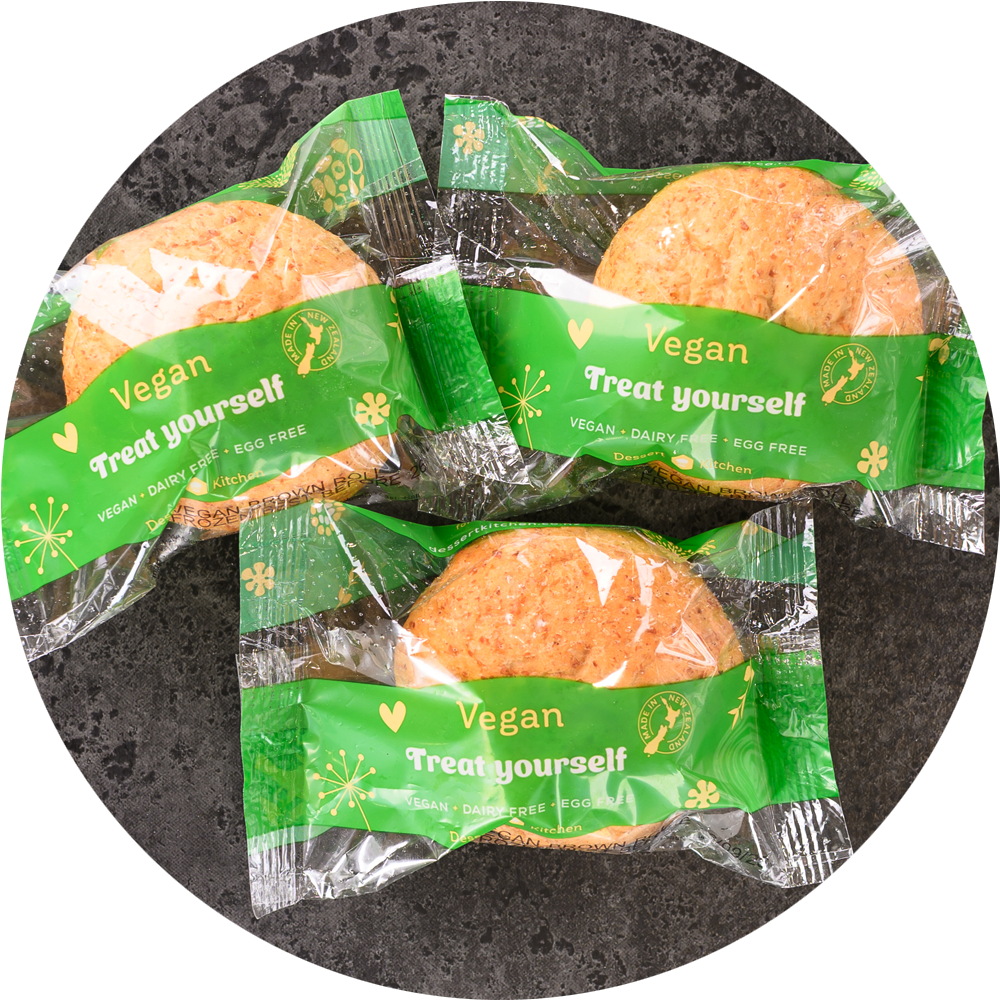 Three vegan cookies in green packaging on a dark textured background. Dessert Kitchen